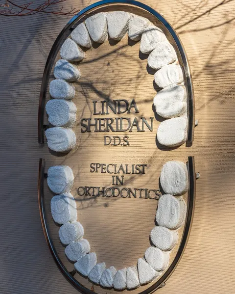 Sign on the practice wall reading Linda Sheridan D.D.S., Specialist in Orthodontics, framed by a sculpture of teeth